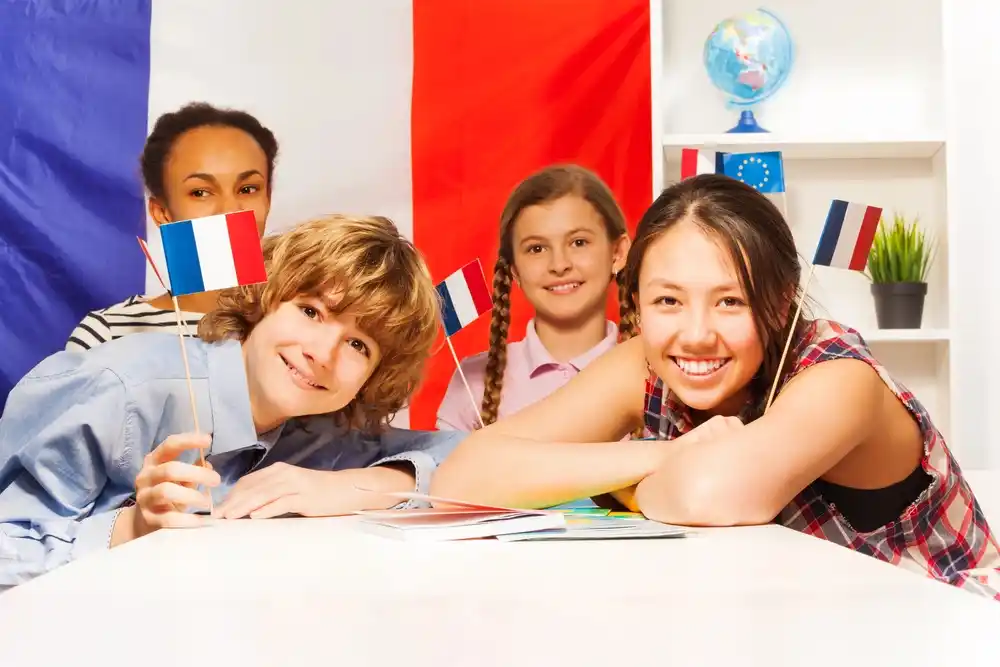 Four diverse students smile, holding small French flags, learning French language.