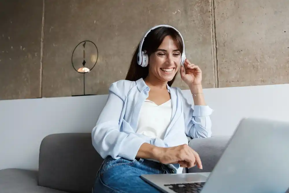 Smiling woman working from home on laptop, wearing headphones.