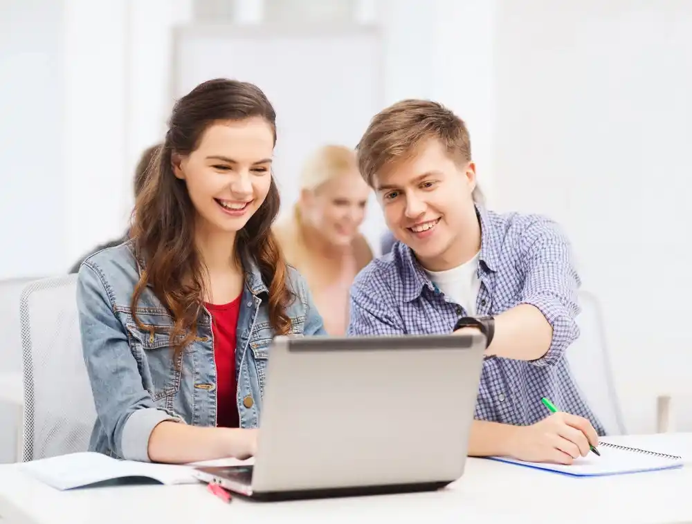Two college students collaborate on a laptop, working together on a project.