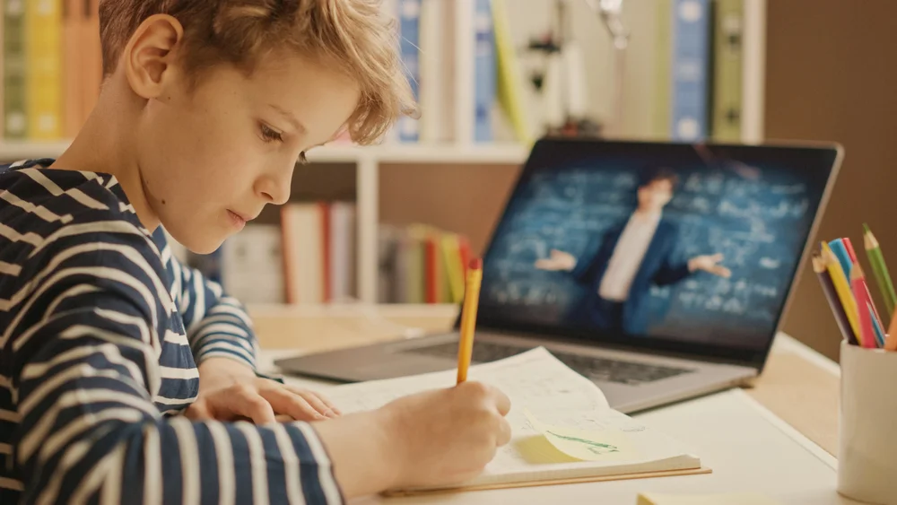 Boy using laptop for online learning, taking notes