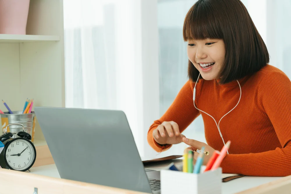 Happy young woman video conferencing on laptop at home office