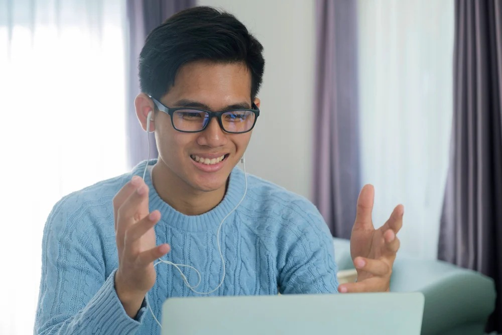 Smiling man in blue sweater video conferencing on laptop