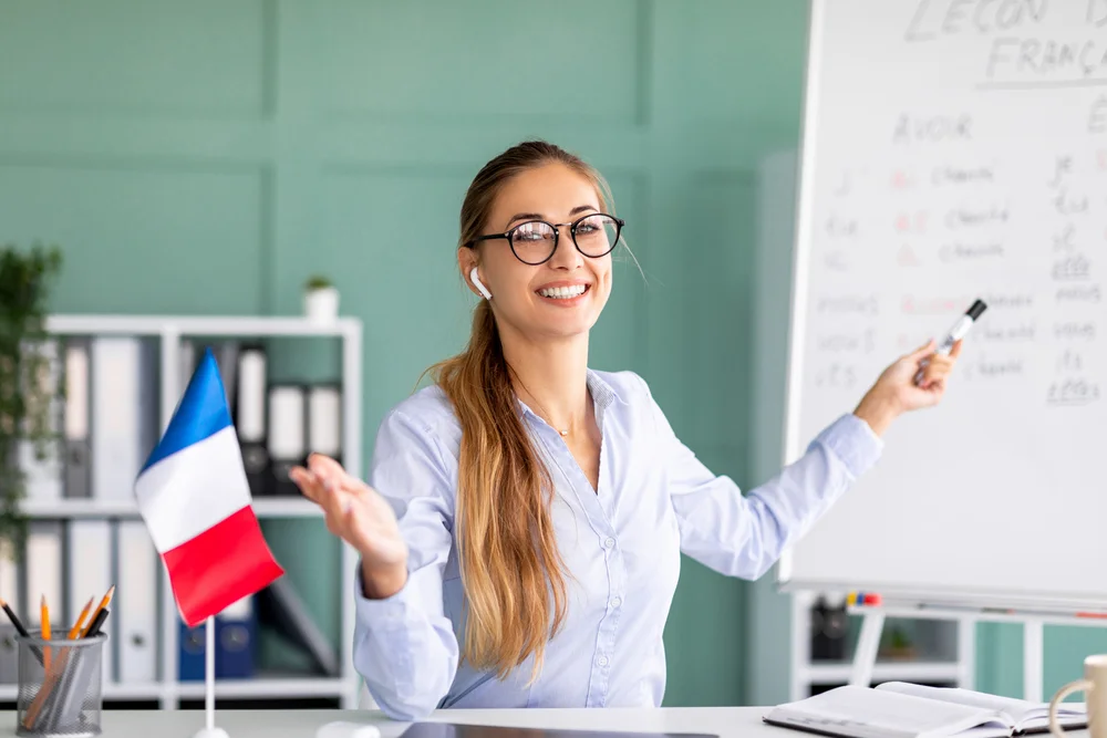 Happy French teacher giving online lesson, pointing to whiteboard with French vocabulary