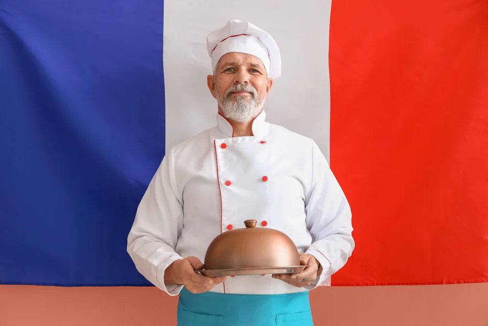Senior French chef presents dish under silver cloche