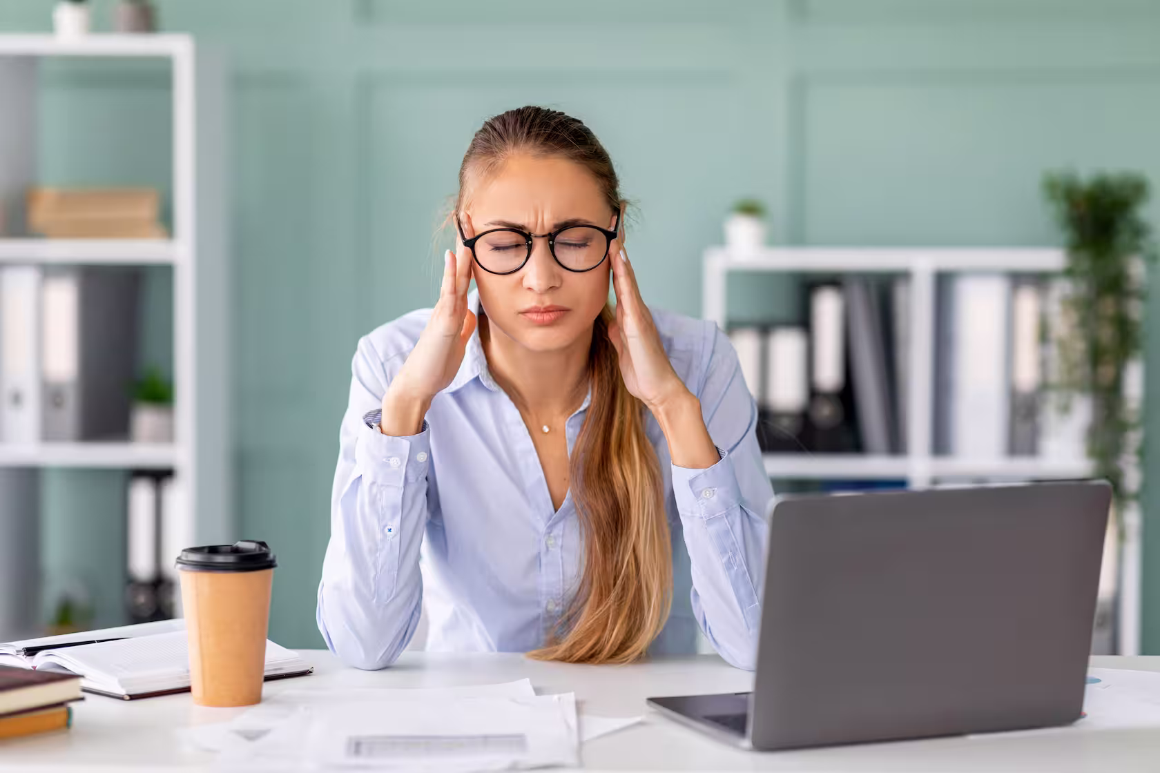 Woman with headache at desk, laptop, and coffee
